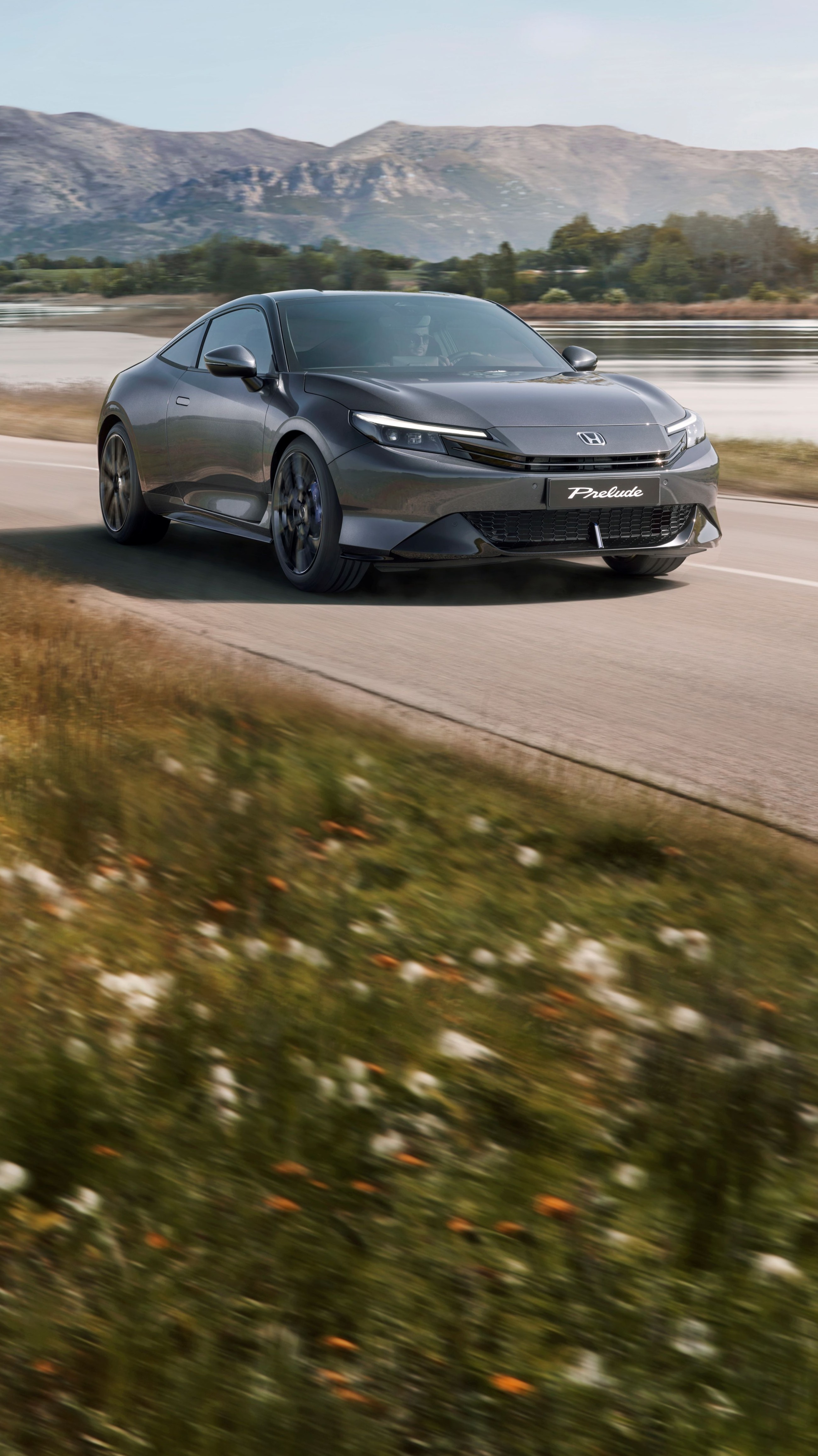 Honda Prelude vo farbe Crystal Black Pearl jazdiaca po kľukatej ceste s voľnou krajinou v pozadí.