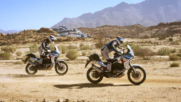 Dvaja jazdci z výpravy HAR v Maroku s maľovanými skalami na pozadí