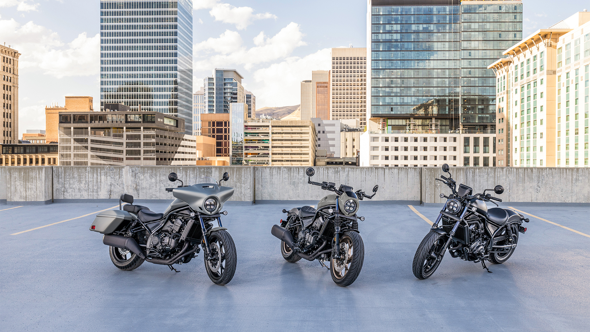 Tri motocykle CMX1100 vonku pred modernými budovami.